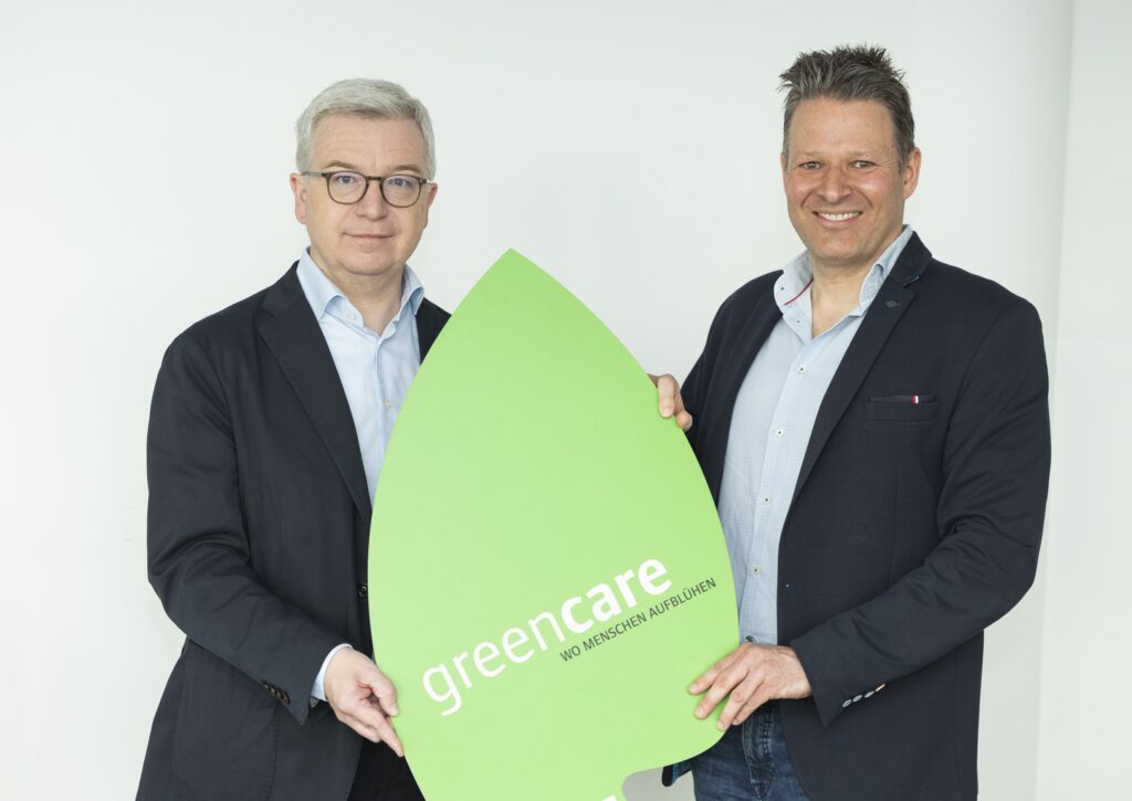 Zwei Männer halten grünes Schild mit Greencare-Logo.