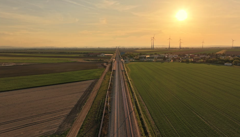 Landschaft mit Gleisen, Feldern und Windrädern bei Sonnenuntergang.