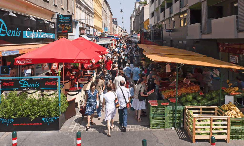 Belebter Marktplatz mit Fruchtständen und Restaurant.