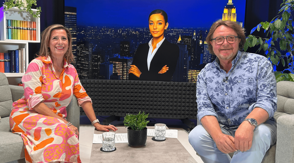 Zwei Personen sitzen und lächeln im Studio mit Bildschirm.