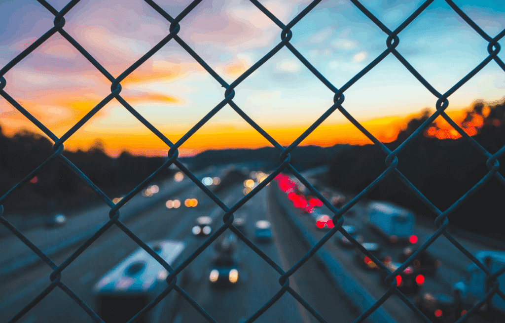 Maschendrahtzaun vor unscharfer Autobahn bei Sonnenuntergang