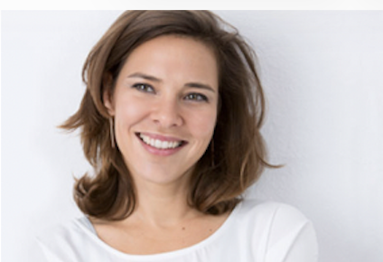 Lächelnde Frau mit braunen Haaren vor hellem Hintergrund