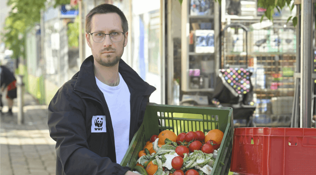 Mann mit Gemüsekiste vor Laden